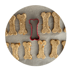 A cookie cutter shaped like a dog bone surrounded by cookies.